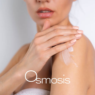 Woman applying Osmosis skincare moisturizer to shoulder showing healthy radiant skin.